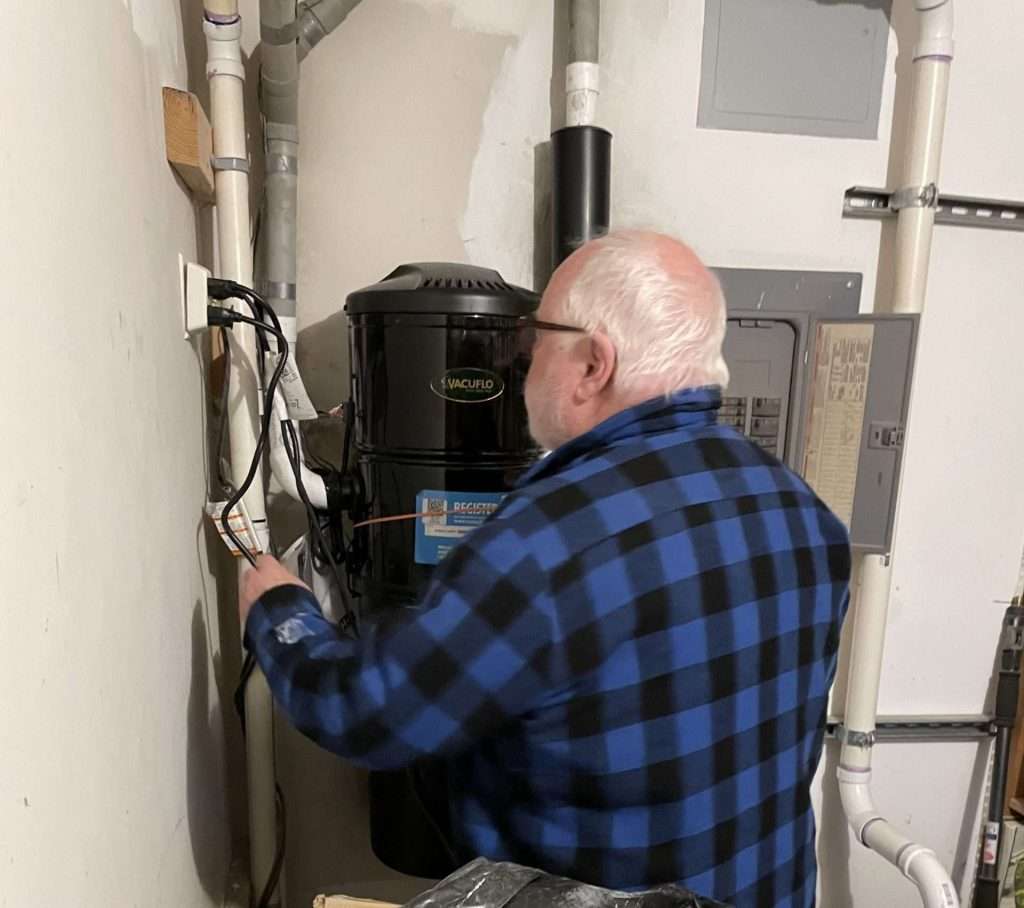 Technician repairing a central vacuum power unit in a residential utility room